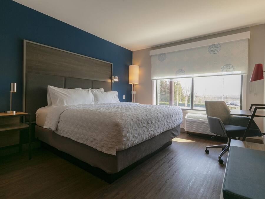 A hotel room with a large bed, a desk, a chair, and a window with blinds.