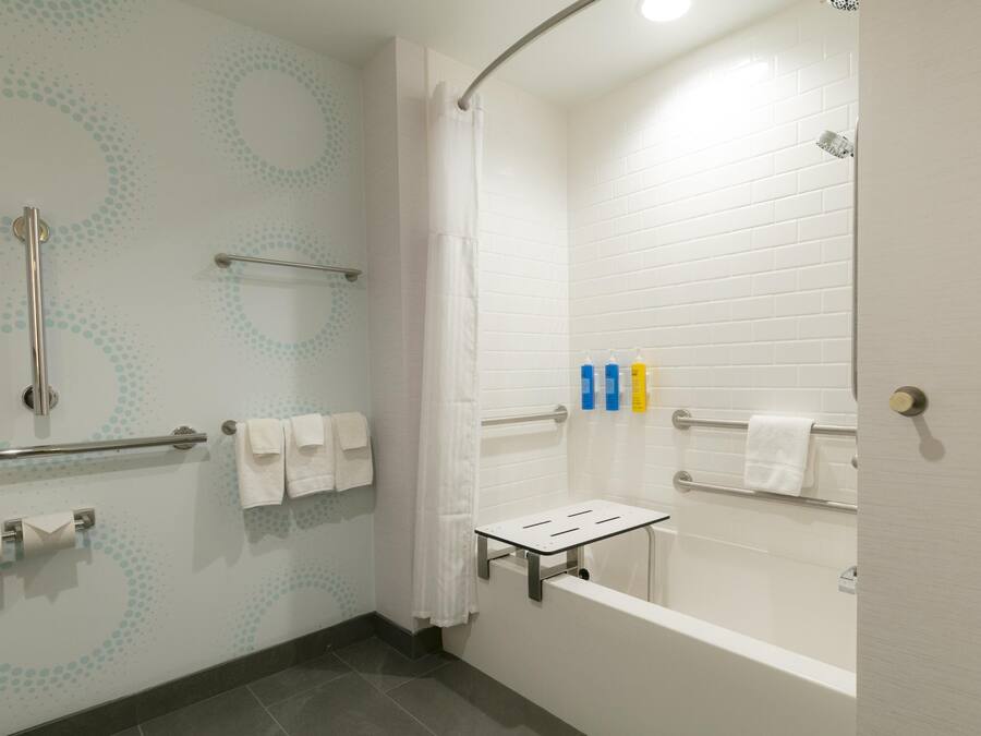 A modern bathroom with a shower, grab bars, a towel rack, and a toilet paper holder.