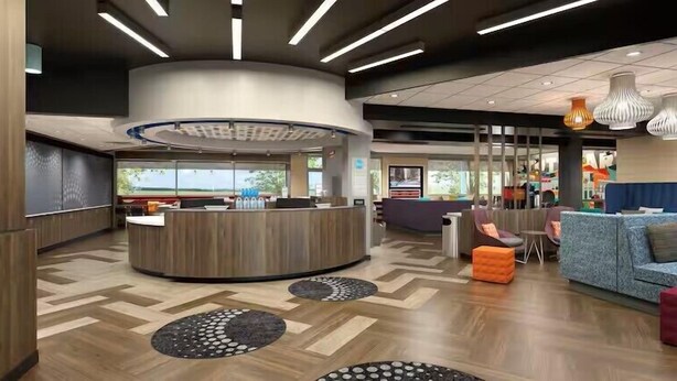 A modern reception area with a curved desk, seating with orange cushions, and patterned floor tiles. - Tru By Hilton Hazleton (Hazleton)