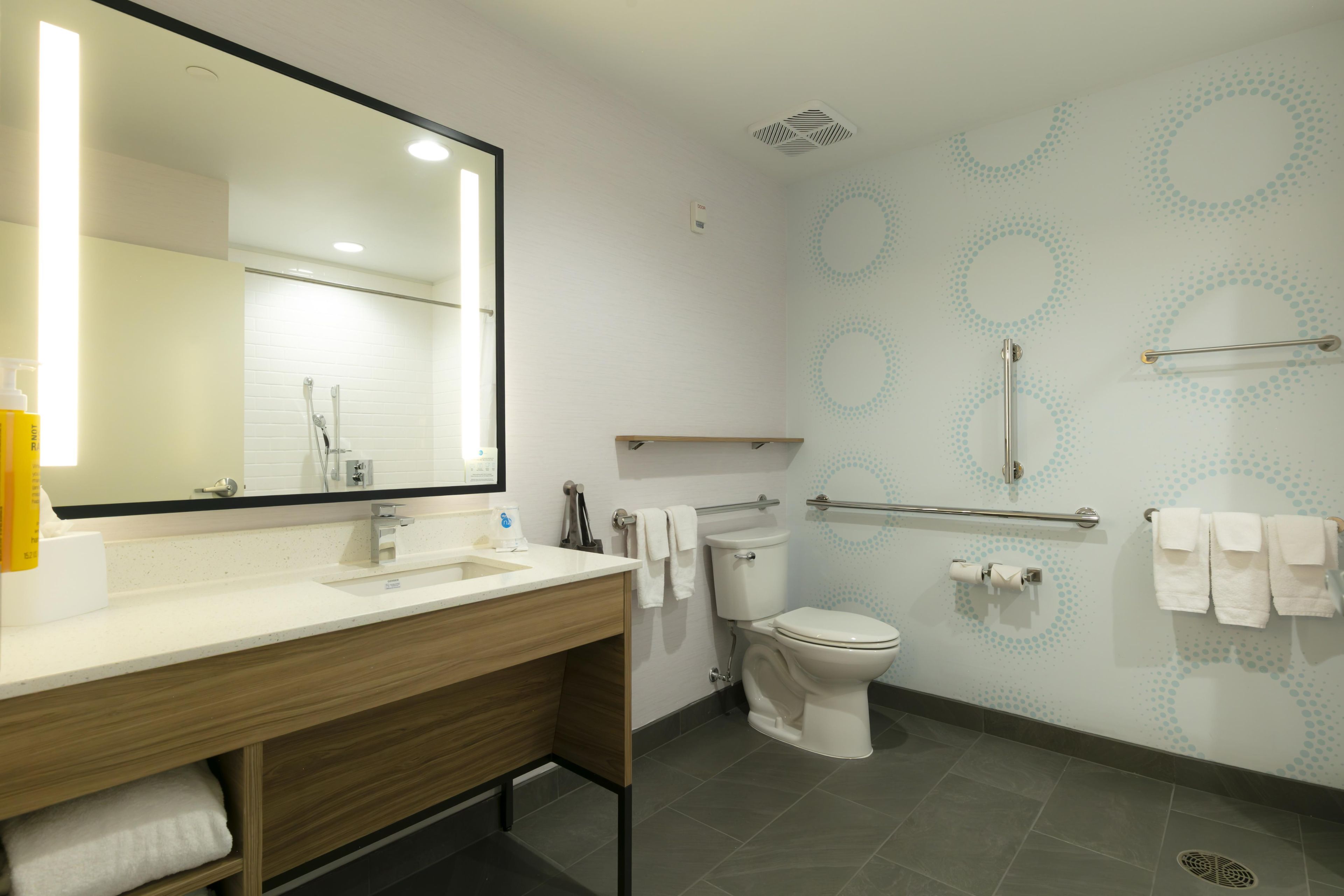 A modern bathroom with a large mirror, a sink, a toilet, and a shower.