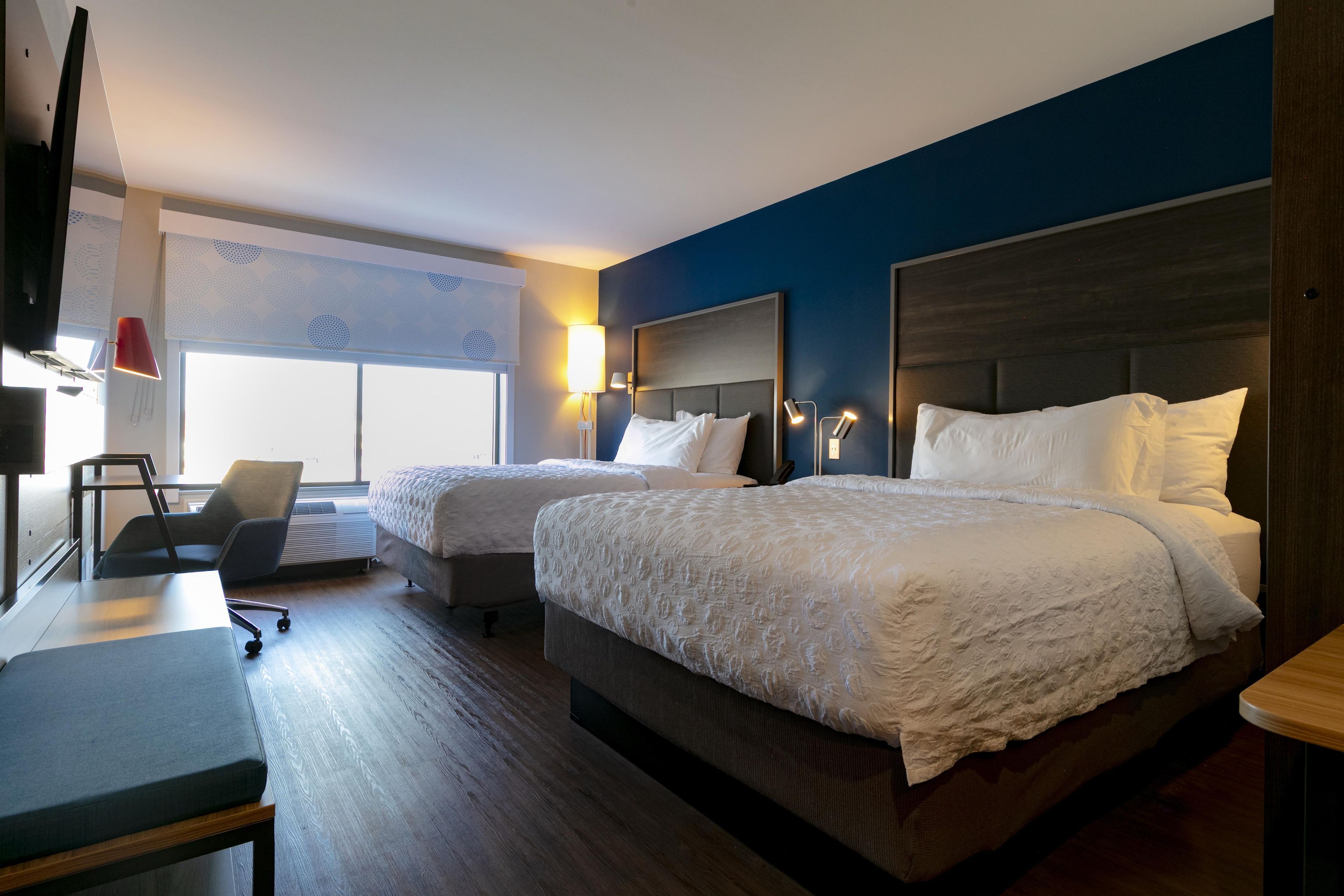 Une chambre d’hôtel avec deux lits, un bureau, une chaise et un téléviseur.
