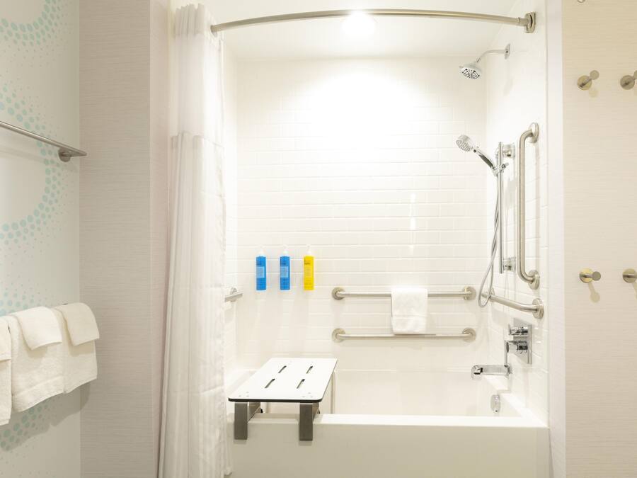 A modern bathroom with a bathtub, shower, and handrails.