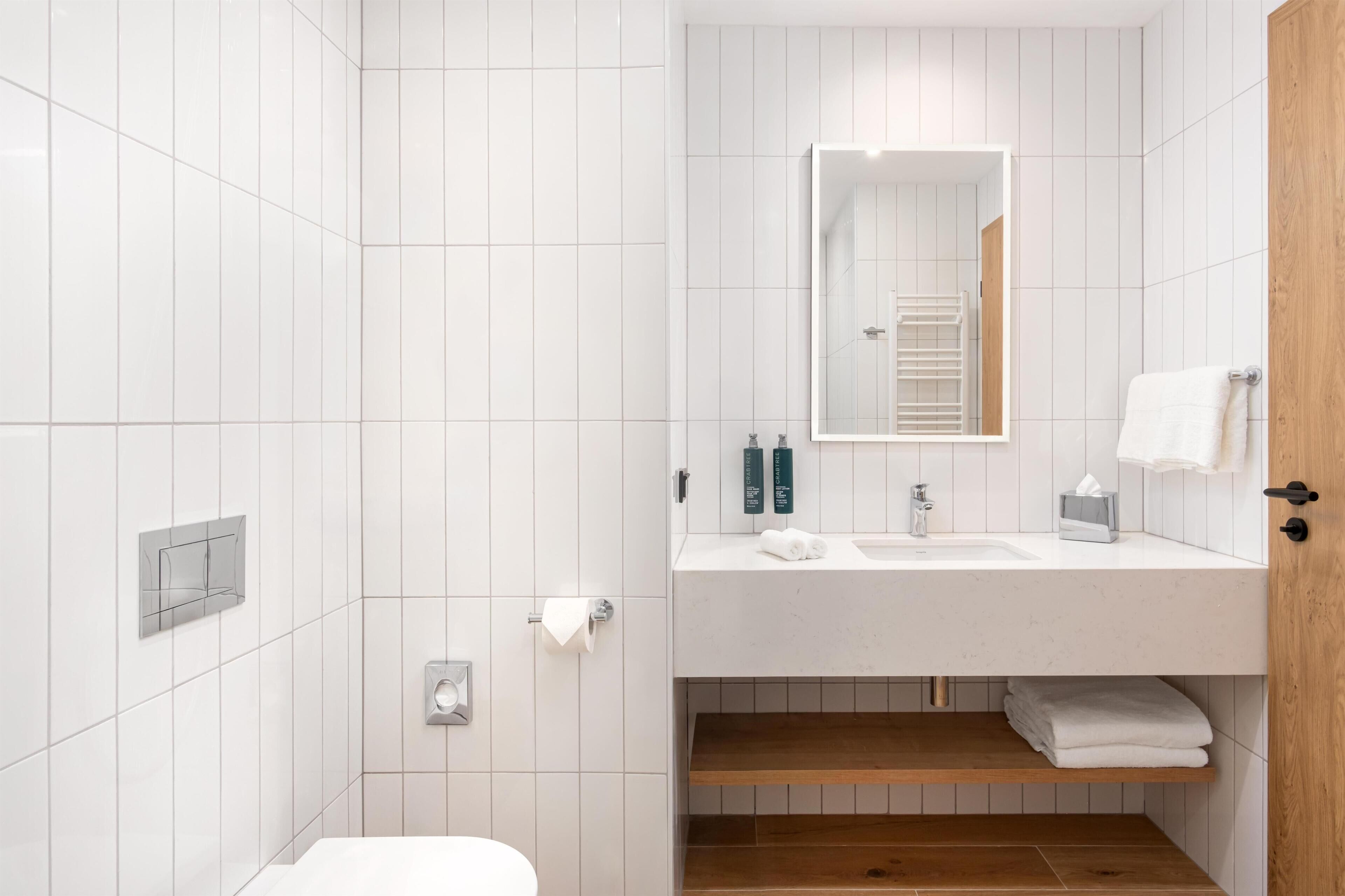 Un bagno moderno con doccia in piastrelle bianche, mobile bagno in legno con specchio e toilette.