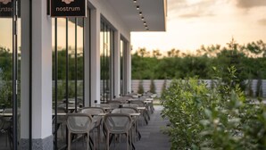 An outdoor dining area with tables and chairs, a sign with the name 'nostrum,' and a view of greenery and a cloudy sky. - Hilton Garden Inn Brasov (Brasov)