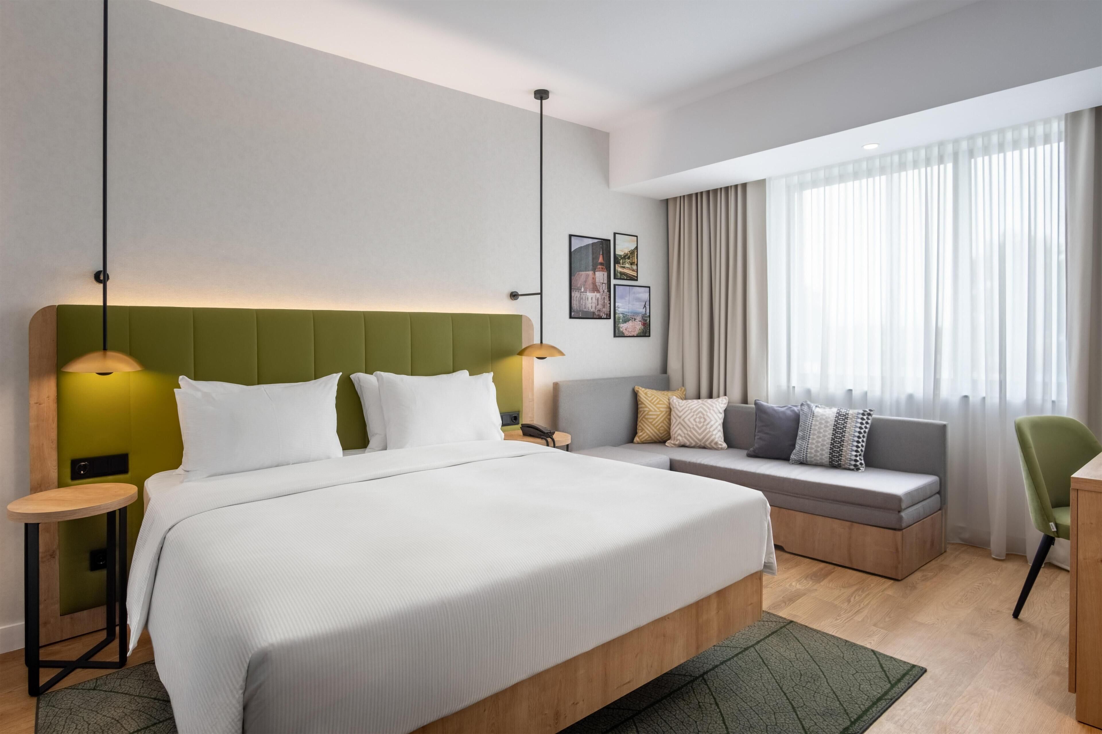 A modern hotel room with a large bed, a sofa, a desk, and a chair.
