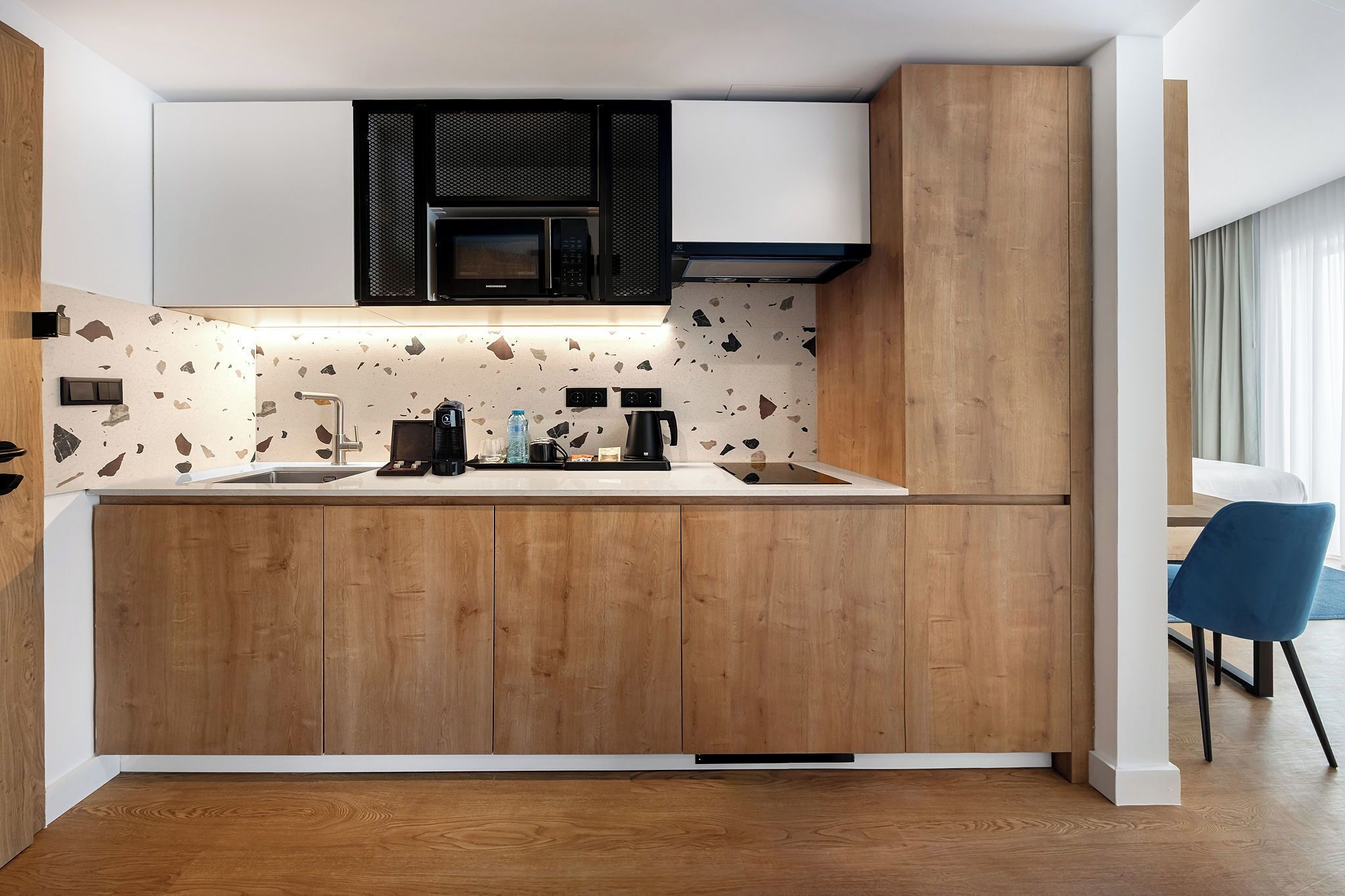 A modern kitchen with wooden cabinets, a white countertop, a black microwave, and a coffee maker.