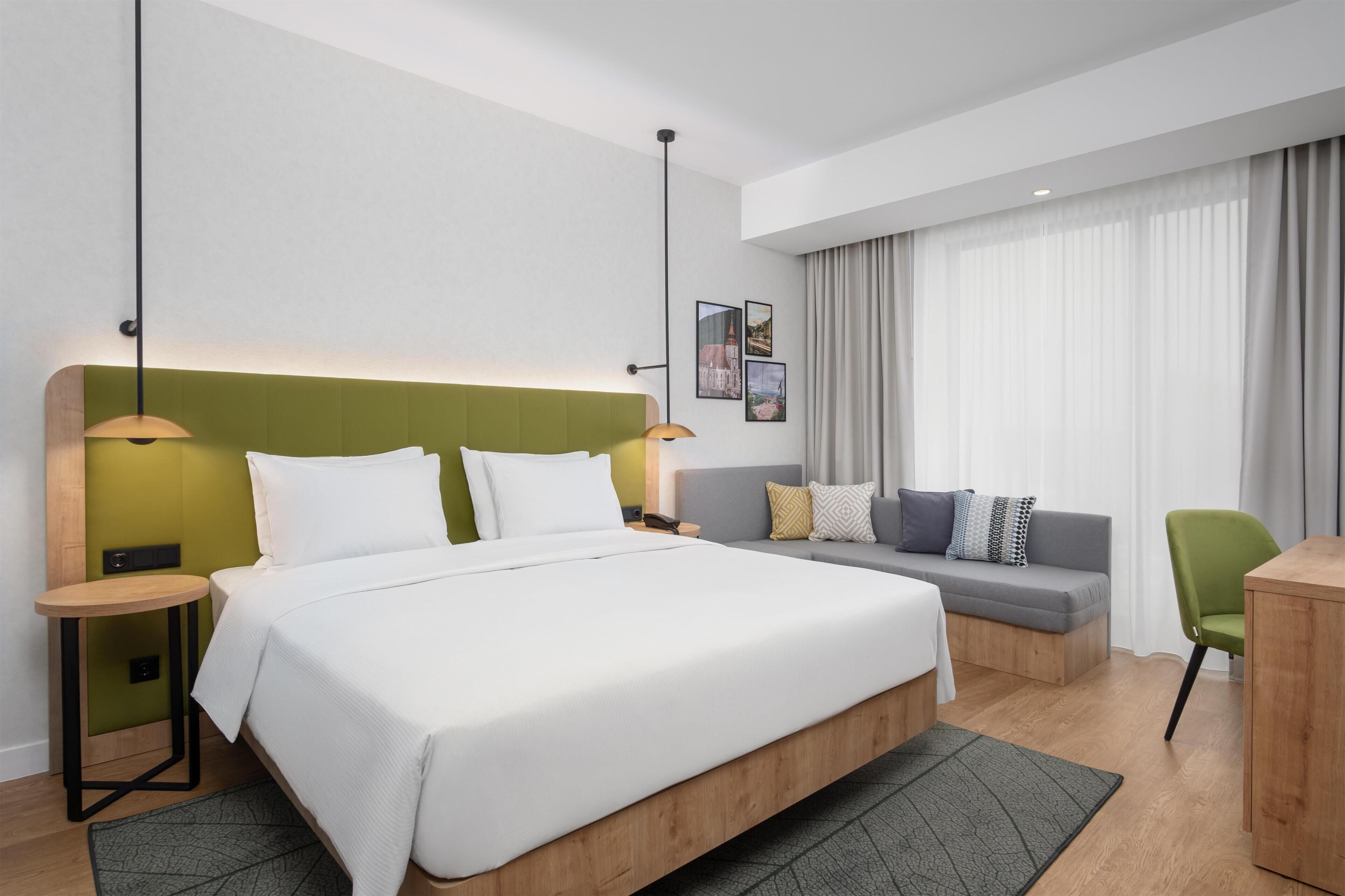 Ein modernes Hotelzimmer mit einem großen Bett, einer Couch, einem Schreibtisch und einem Sessel.