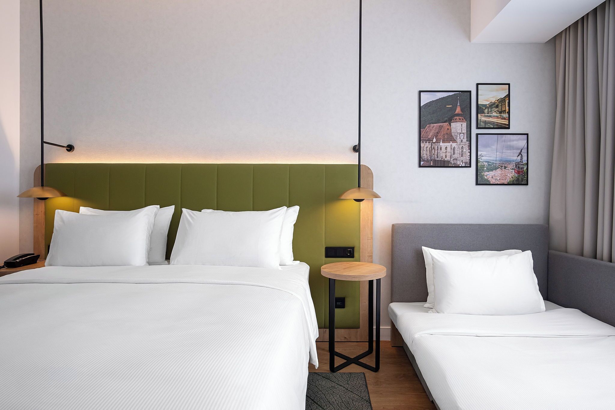A hotel room with a bed, a smaller bed, a nightstand, a lamp, and two framed pictures on the wall.