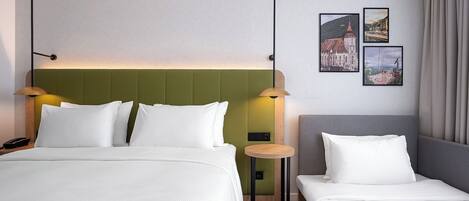Une chambre d’hôtel avec un lit, un petit lit, une table de chevet, une lampe et deux tableaux encadrés au mur.