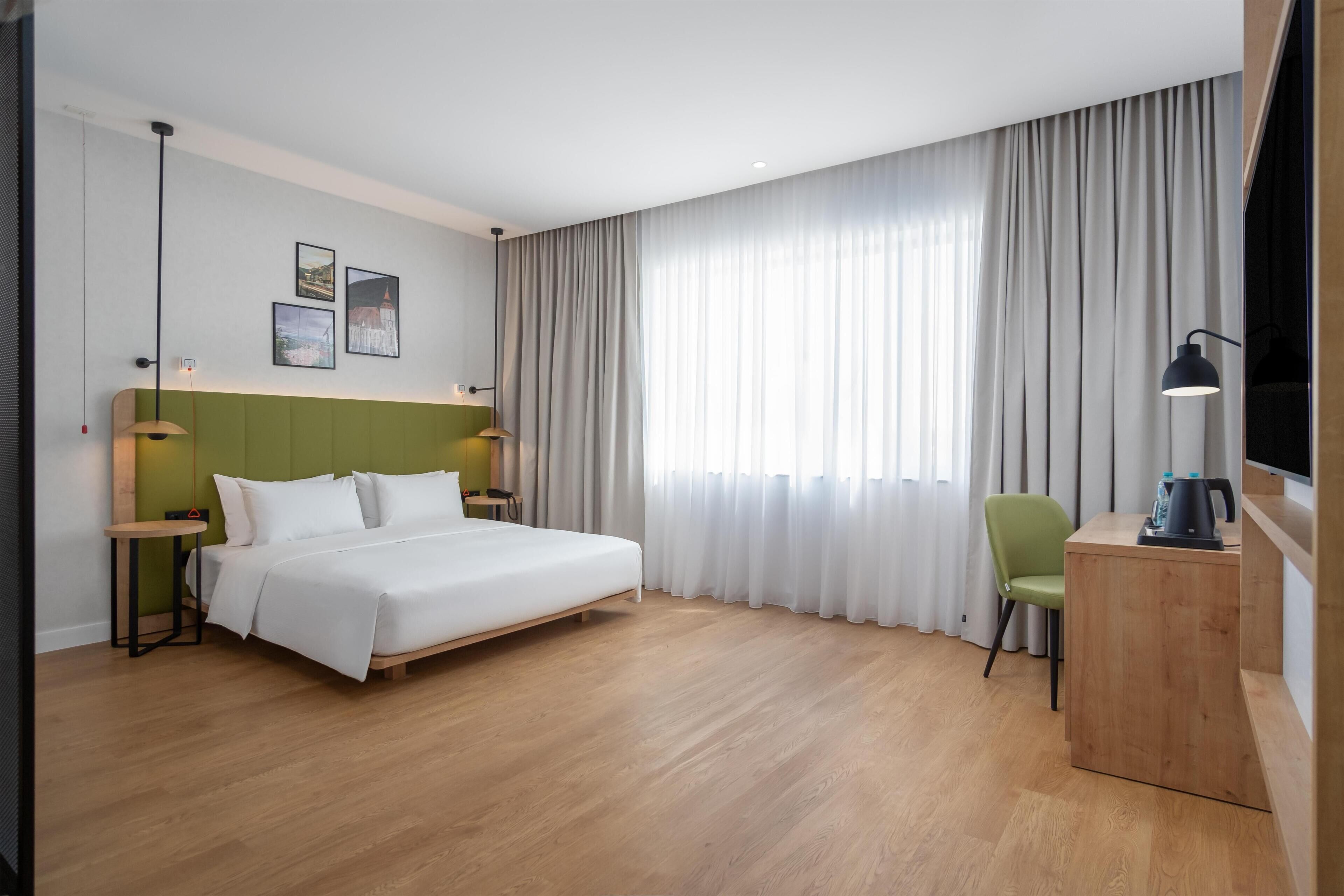 A modern hotel room with a bed, a desk, a chair, and a TV.