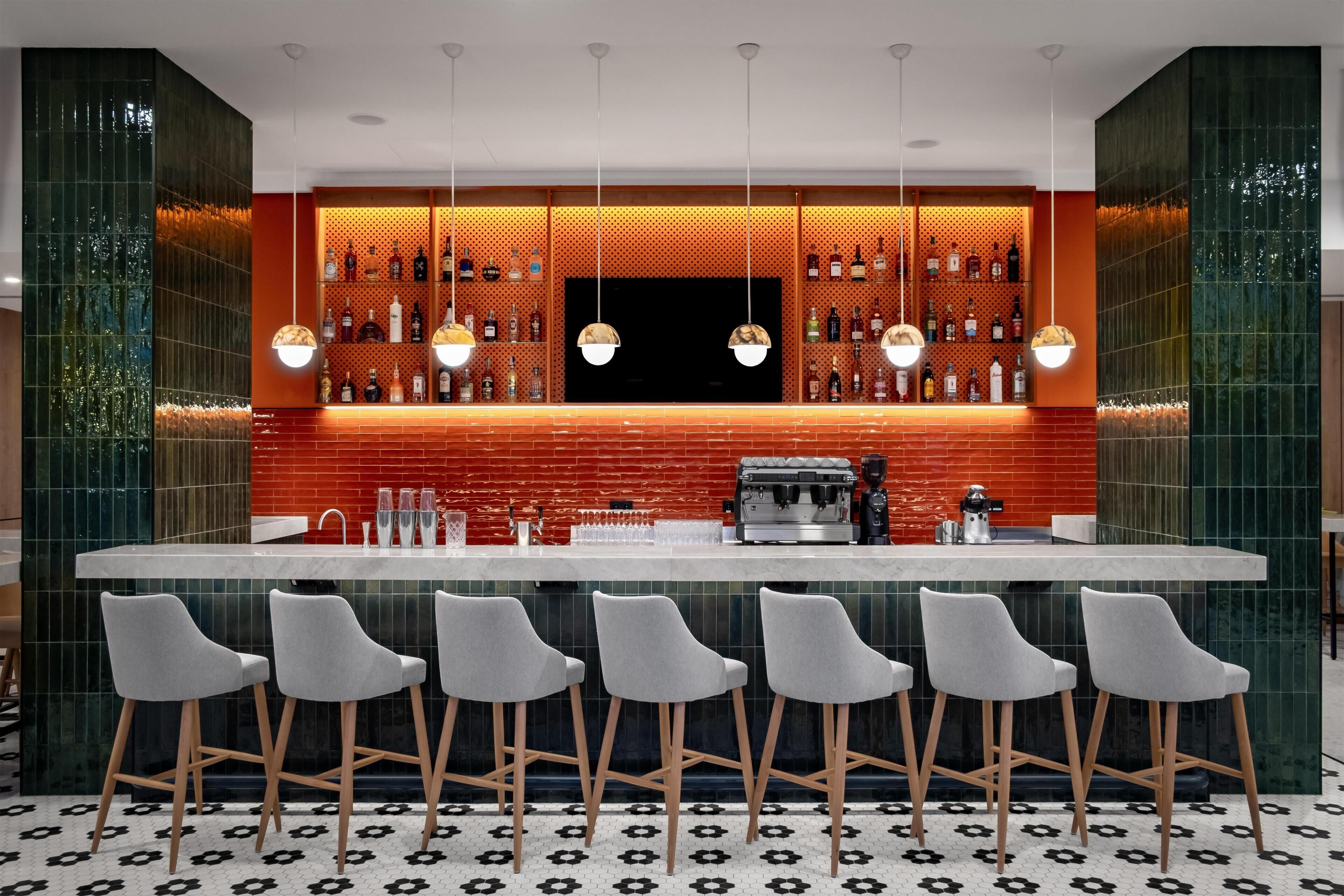 A bar area with a red tiled backsplash, multiple hanging pendant lights, and a coffee machine.