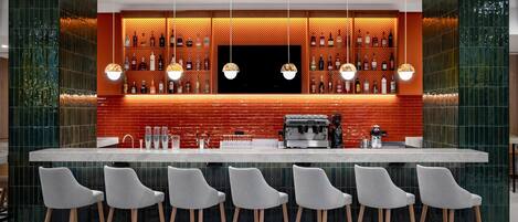 A bar area with a red tiled backsplash, multiple hanging pendant lights, and a coffee machine.
