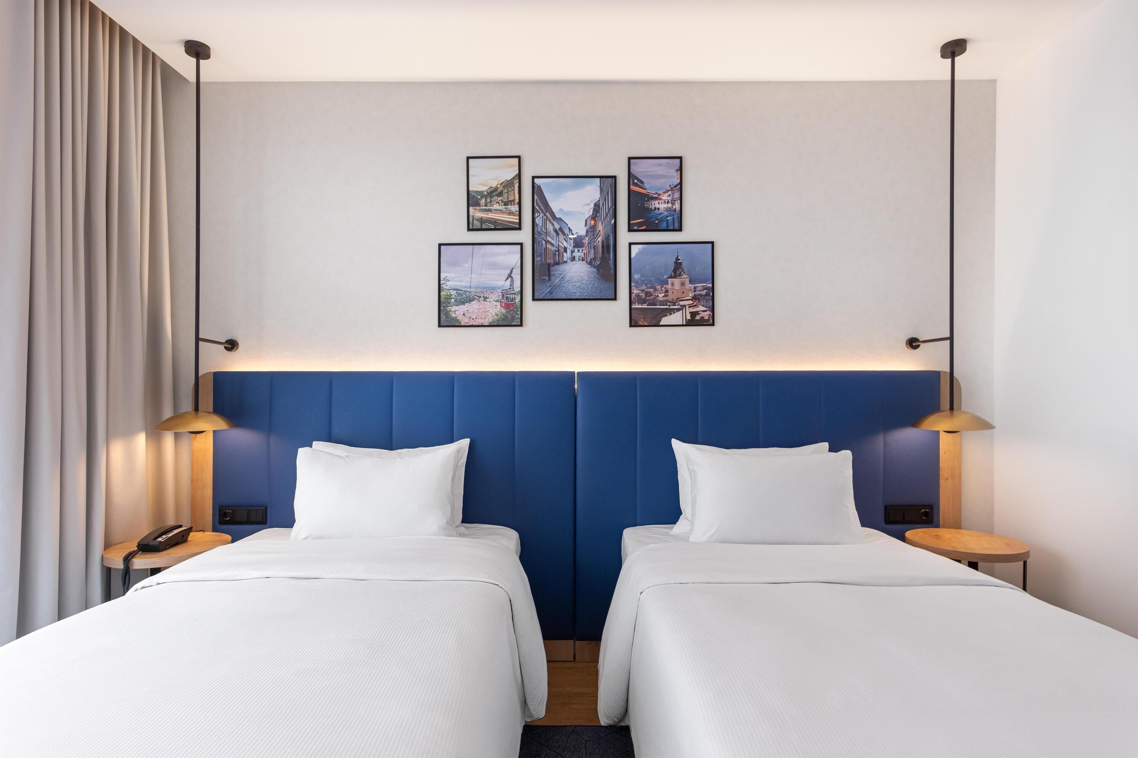 A hotel room with two beds, a blue headboard, a wall-mounted phone, and framed pictures.