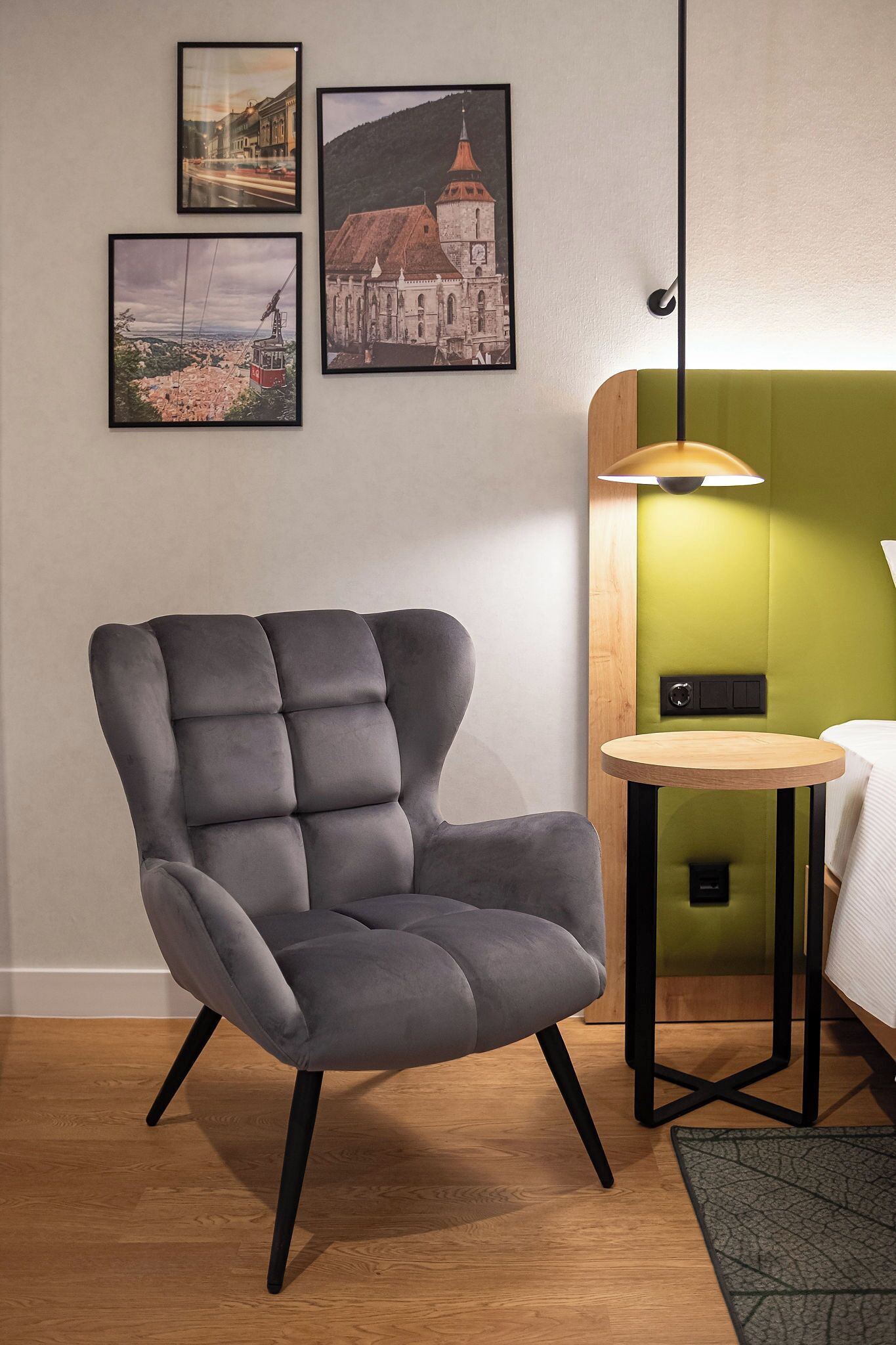 A modern room with a grey upholstered armchair, a round wooden side table, and a green accent wall.