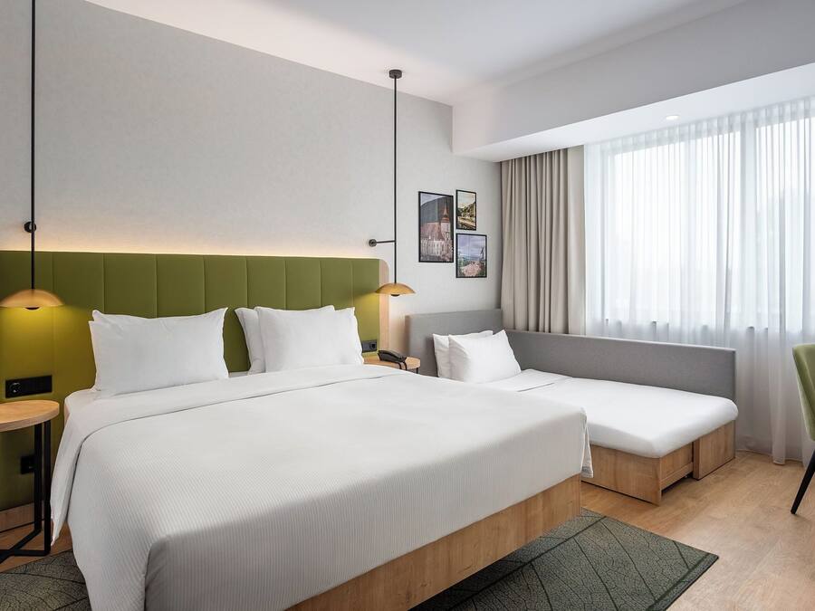 A hotel room with two beds, a desk, a chair, and a large window with curtains.