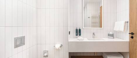 Un baño moderno con azulejos blancos, una puerta de madera, un lavamanos con espejo y un perchero para toallas.