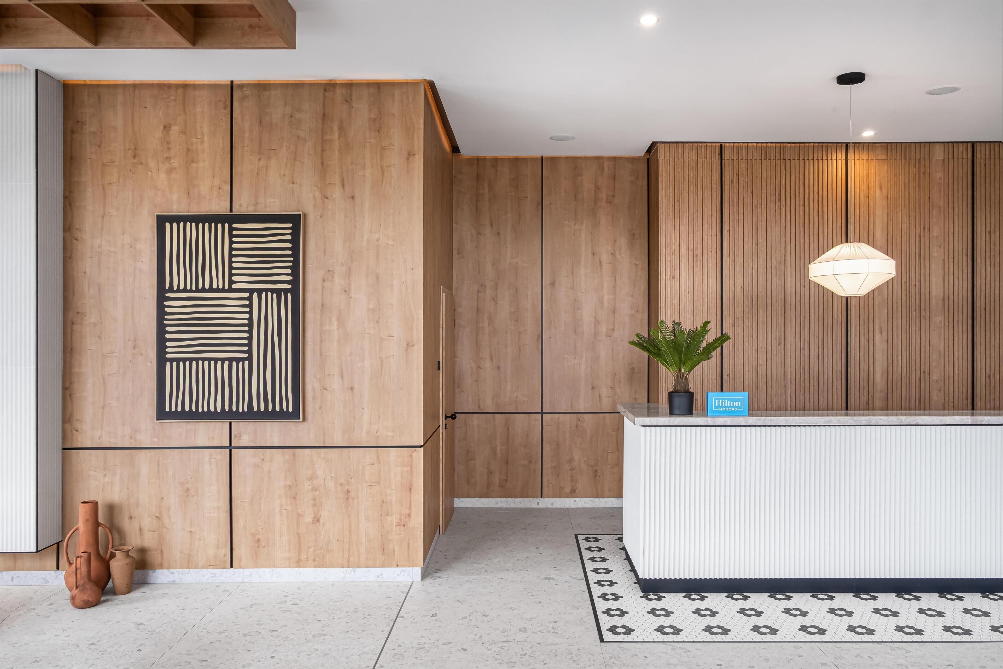 Un área de recepción con pared de madera, un mostrador moderno, una planta en maceta y una alfombra estampada.
