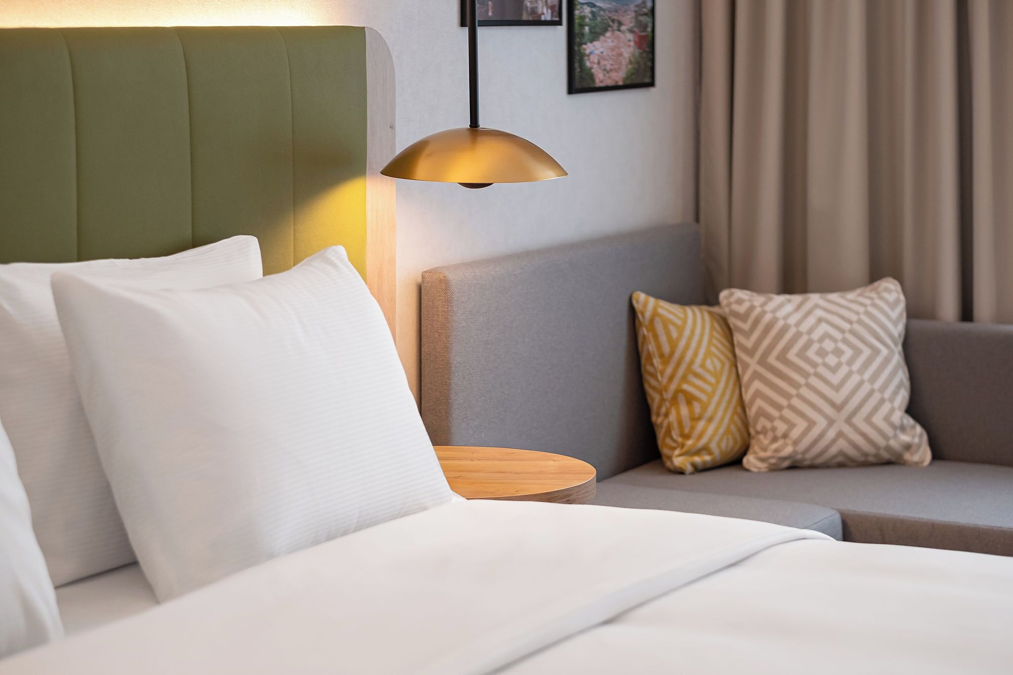 A hotel room with a bed, a nightstand, a sofa, and a pendant light.