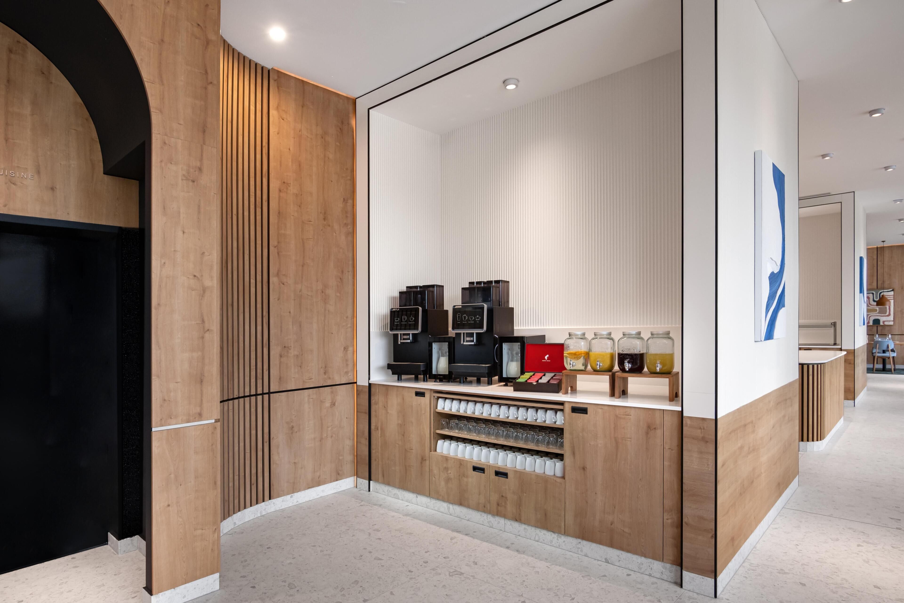 A modern coffee station with espresso machines, a coffee bar, and a display of coffee mugs and jars.