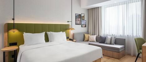 A hotel room with a large bed, a sofa, a chair, a small table, and a window with curtains.