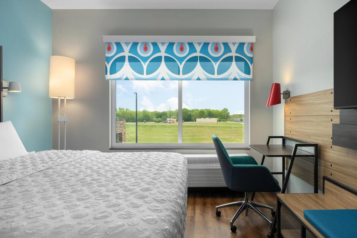 Habitación de hotel con una cama grande, un escritorio, una silla y una ventana con vistas a un paisaje verde.