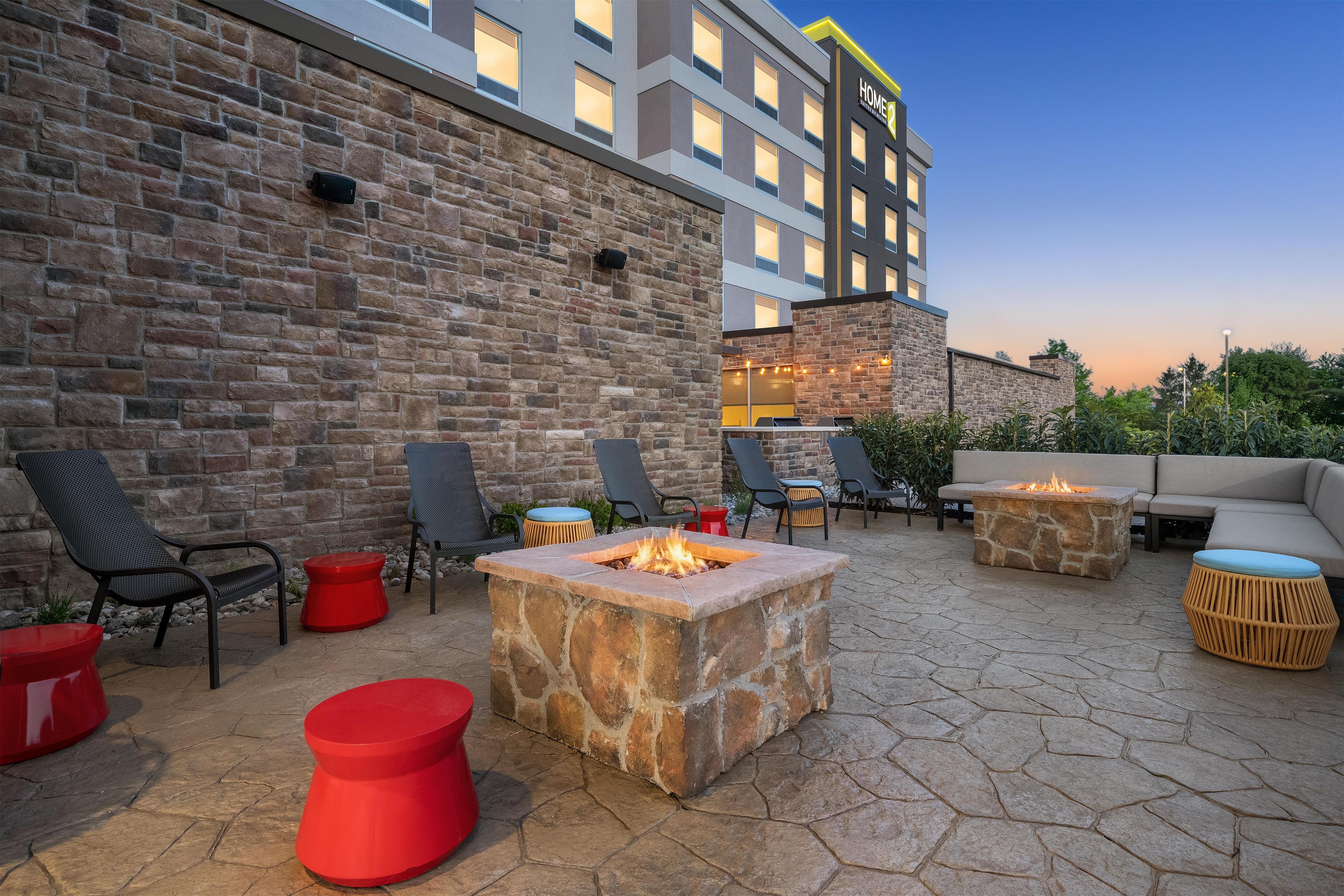 An outdoor patio with stone fire pits, lounge chairs, and a building in the background.