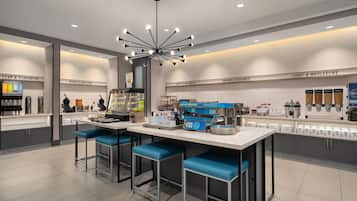 A modern kitchen area with bar stools, a coffee station, and a variety of food dispensers.