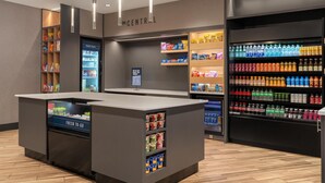 A modern refreshment area with a central counter, refrigerated freezers, and shelves stocked with snacks and beverages. - Tru By Hilton Burlington, Nj (Burlington)