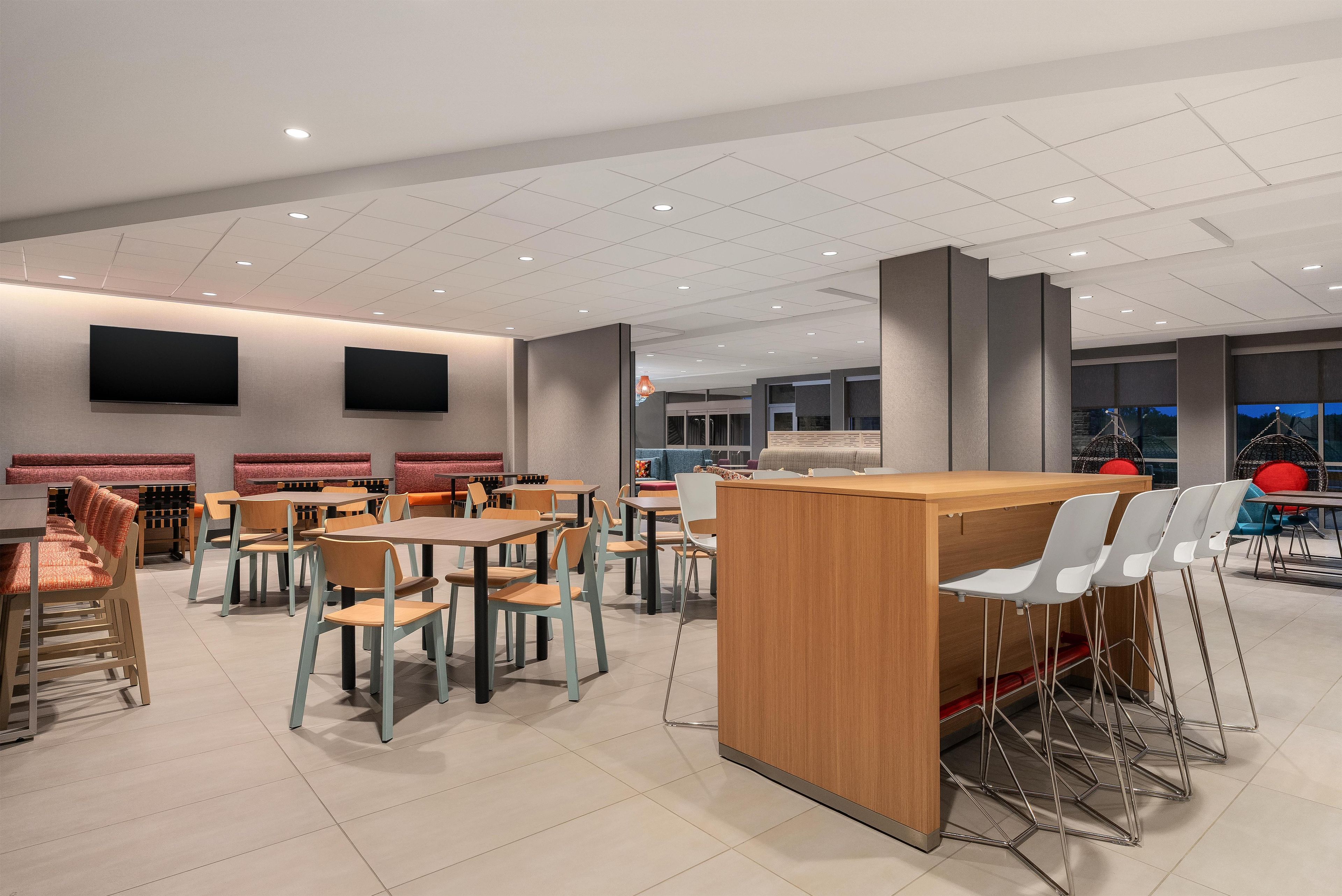 Un restaurant moderne doté de nombreuses tables et chaises, d’un comptoir en bois et d’un éclairage encastré au plafond.