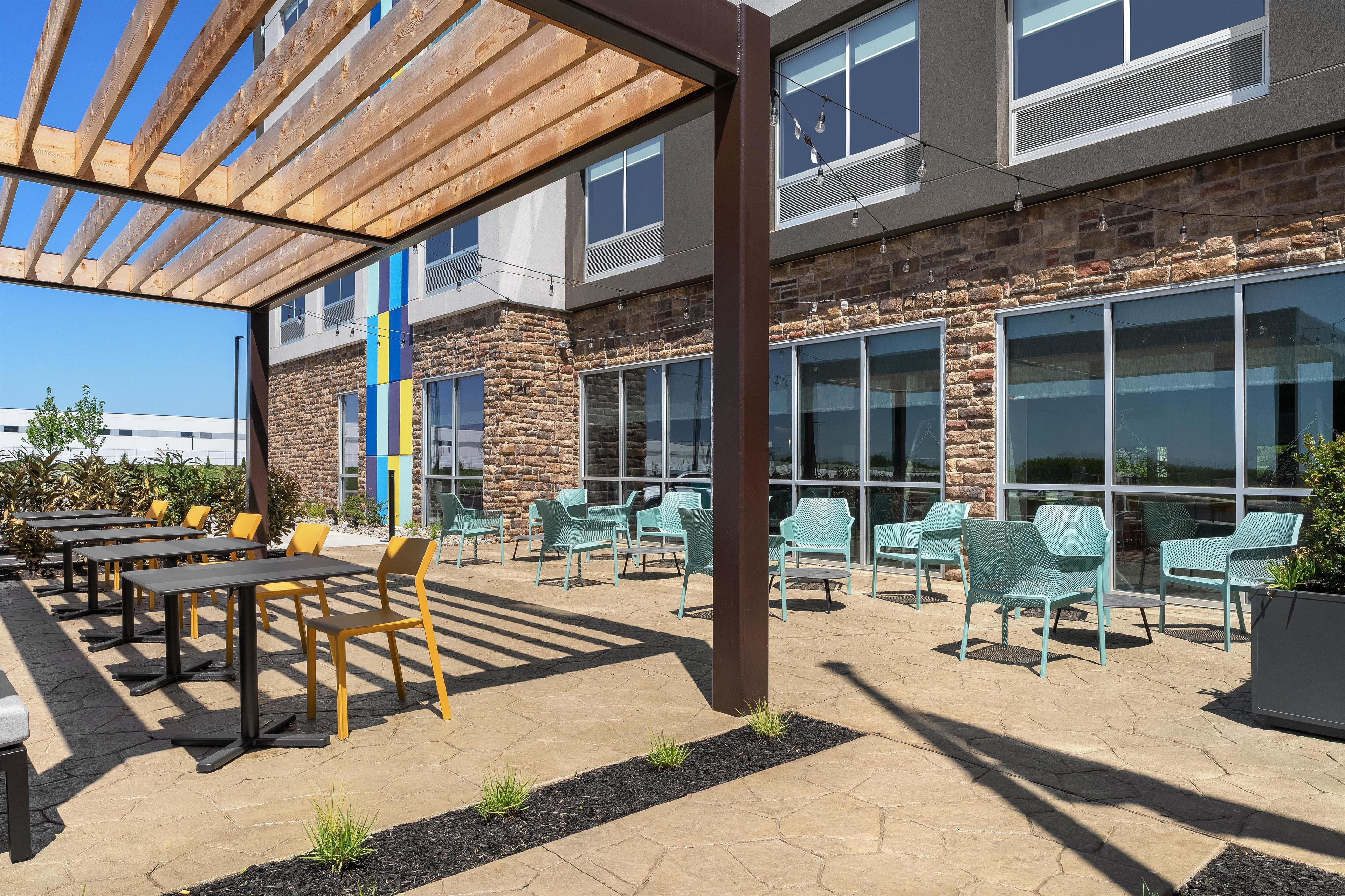Un patio al aire libre con mesas y sillas, una pérgola y un edificio de piedra con ventanas grandes.