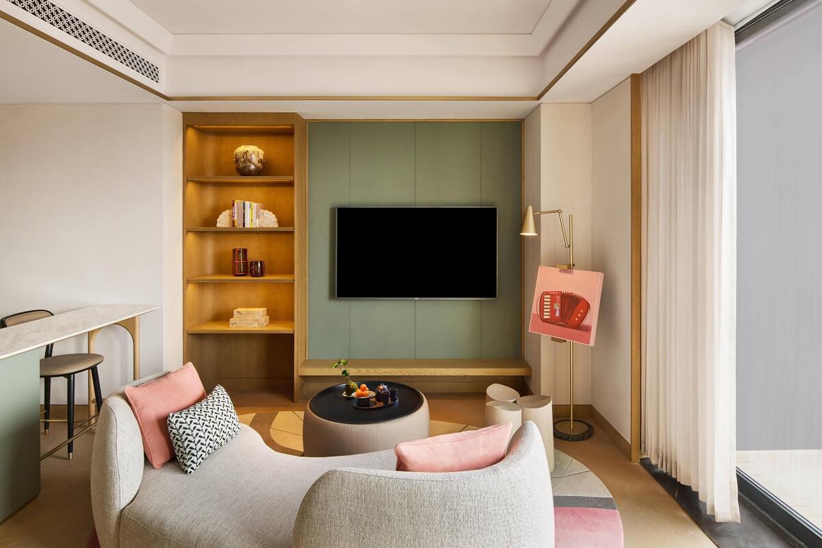 A modern living room with a flat-screen TV, a round coffee table, a sofa with cushions, a bookshelf, and a floor lamp.