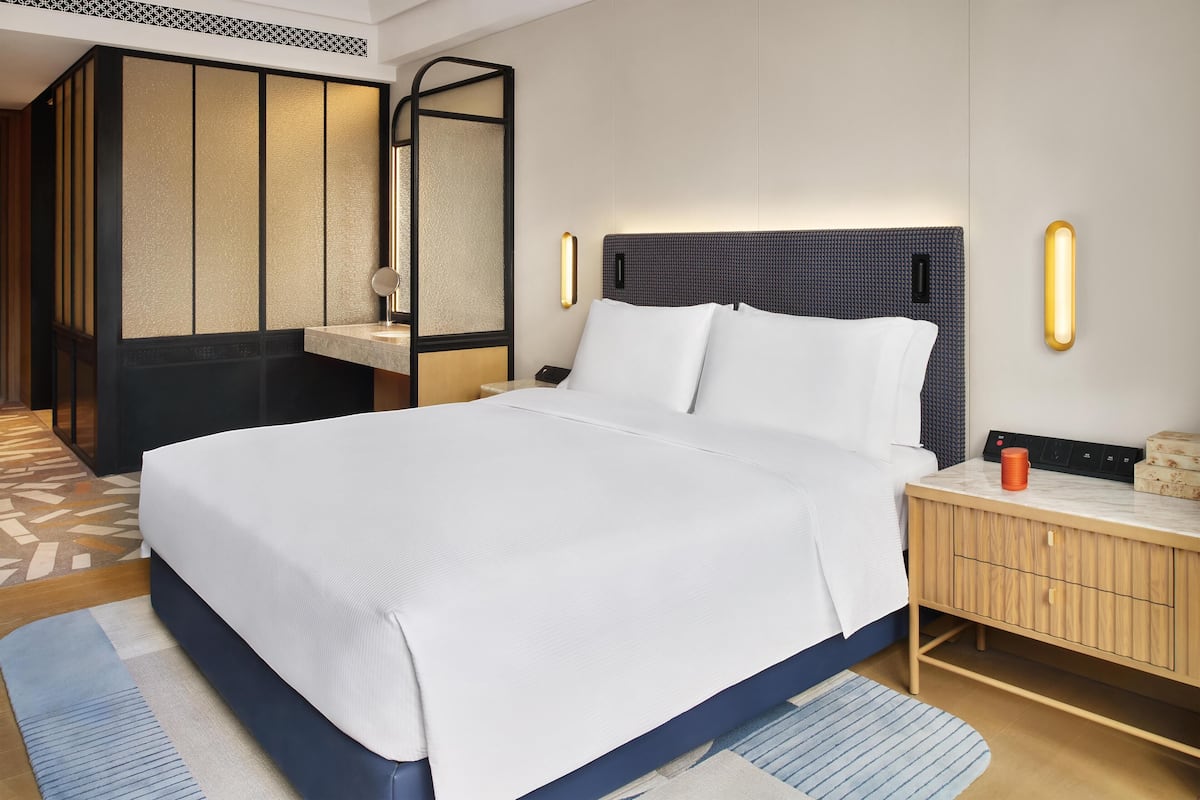 A hotel room with a bed, bedside table, and a mirror.