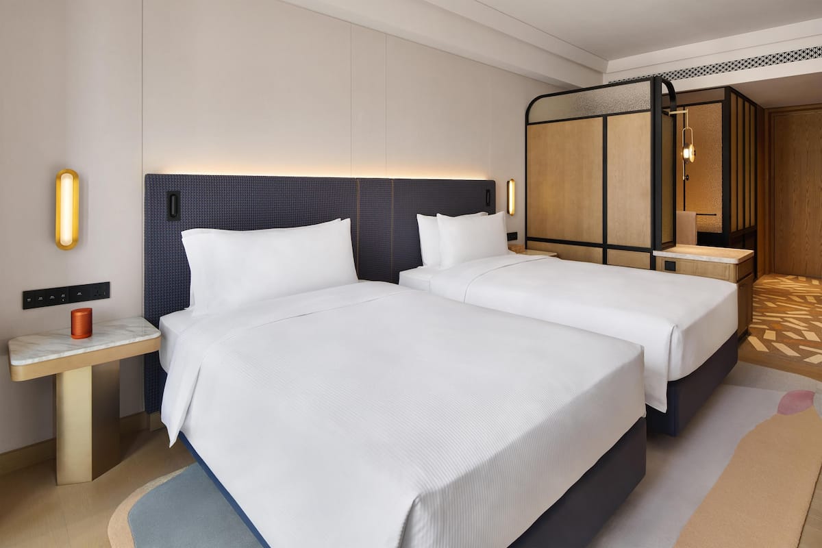 A hotel room with two beds, a nightstand, a mirror, and a patterned rug.
