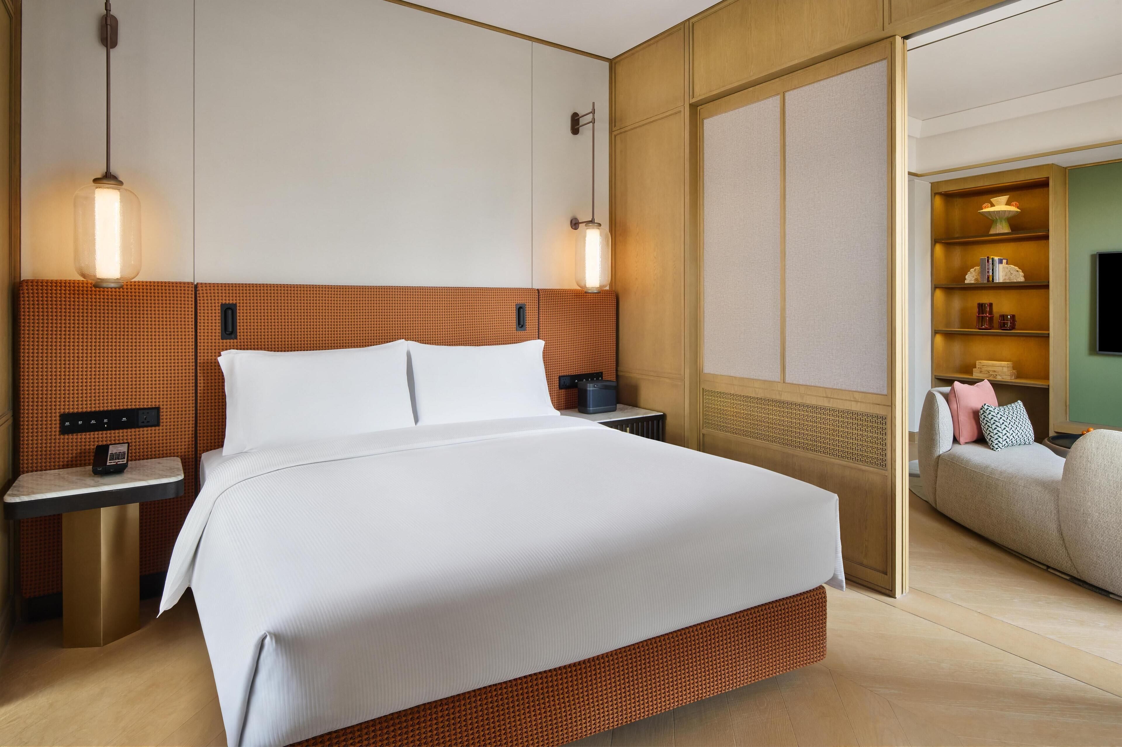 Een hotelkamer met een groot bed, nachtkastjes, een telefoon, een wandplank met decoratieve objecten en een televisietoestel.