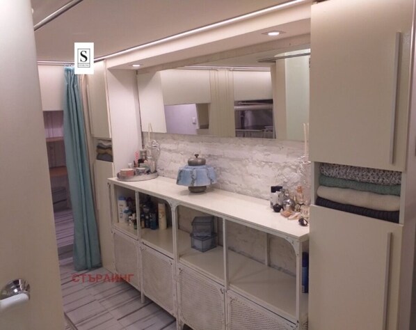 A modern bathroom with a marble countertop, a sink, and a mirror. There are cabinets below the countertop and a shower area visible in the background.
