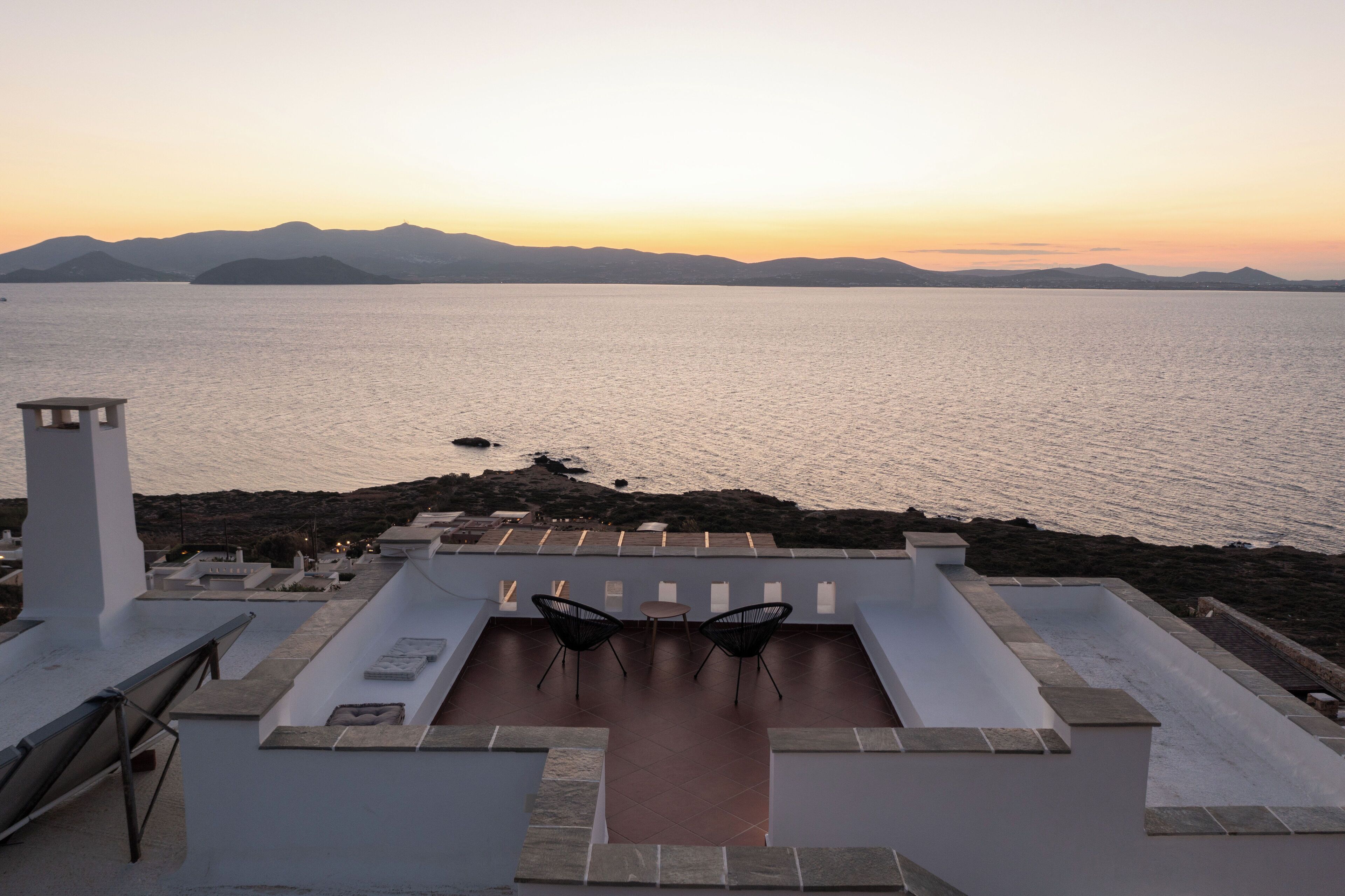 A rooftop terrace with a view of the sea and mountains, featuring a table and chairs.