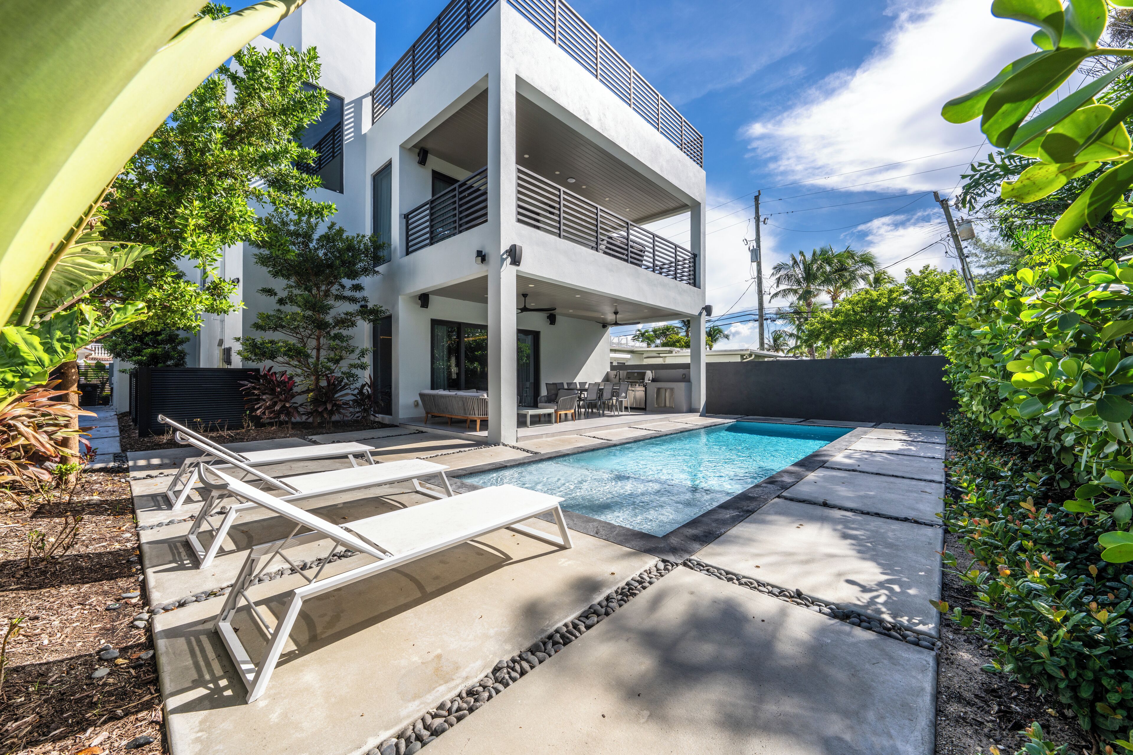 A modern two-story house with a swimming pool, outdoor seating, and lush greenery.
