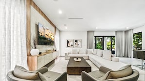 A modern living room with a sectional sofa, two armchairs, a coffee table, and a large window with curtains. - Ocean Crown Villa - A Modern Beach Getaway (Fort Lauderdale)