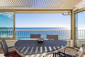 A balcony with a view of the ocean, a round table with a bowl, wicker chairs, and a striped ceiling. - Bright Apartment with Terrace and Sea View (Cannes)