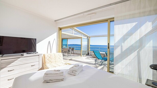 Una camera d'albergo con un letto, una TV, un balcone con vista sul mare e una zona salotto.
