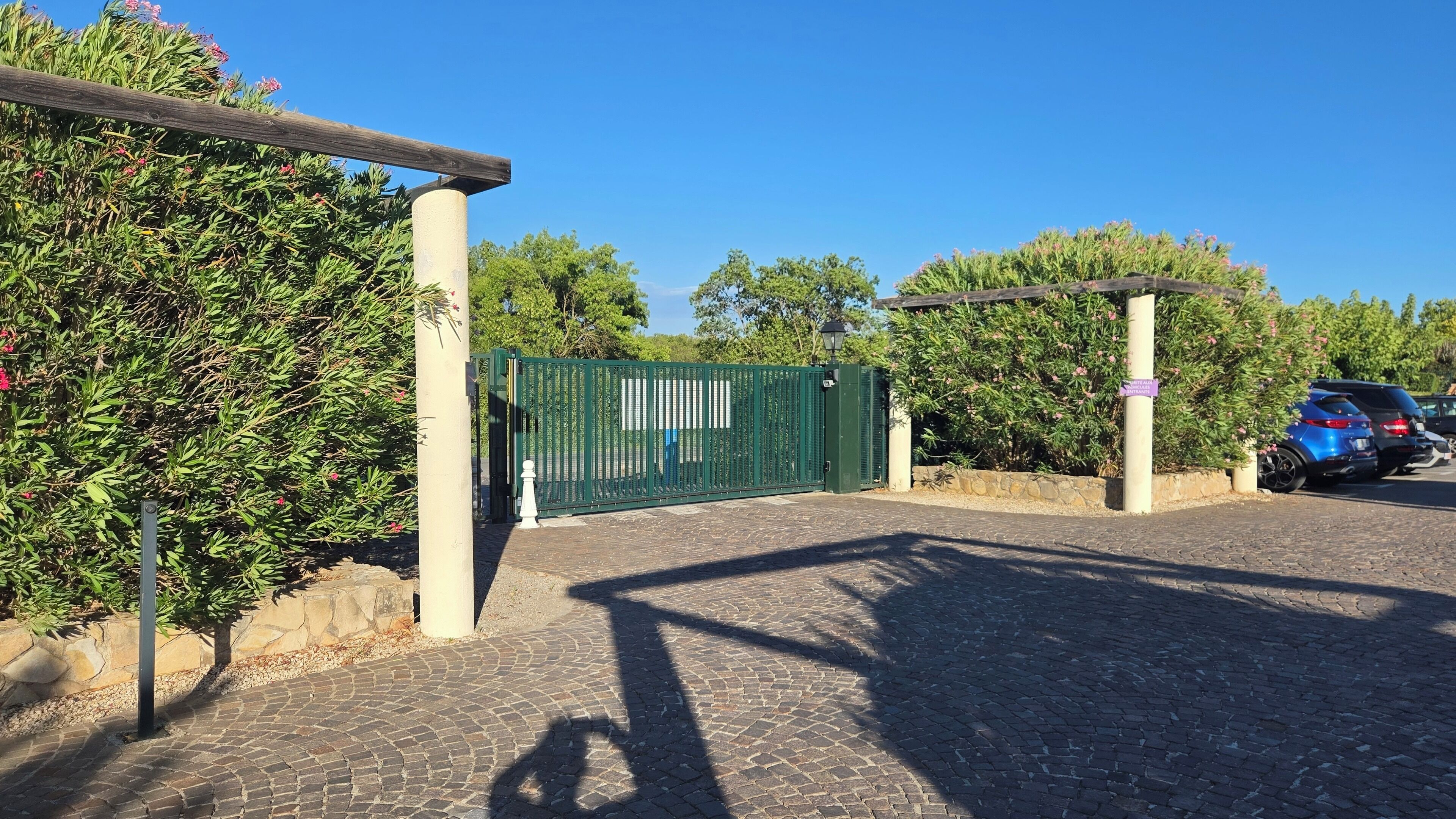 A paved entrance with a green gate, a wooden pergola, and a stone wall.
