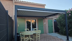 A covered patio with a table and chairs, a green door, and a small garden area. - The yellow house (Vidauban)