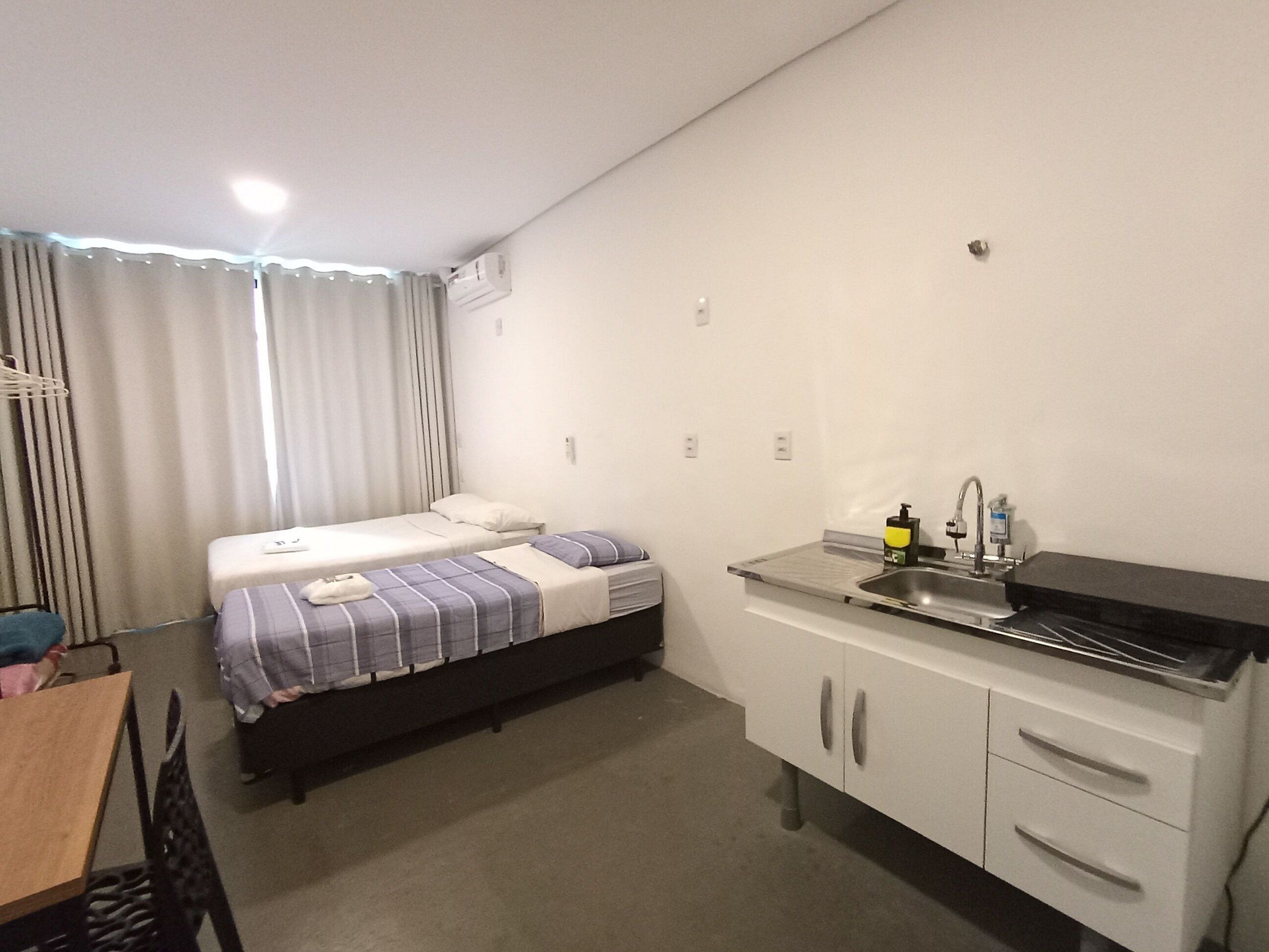 A small, clean room with a bed, a desk, and a kitchenette.