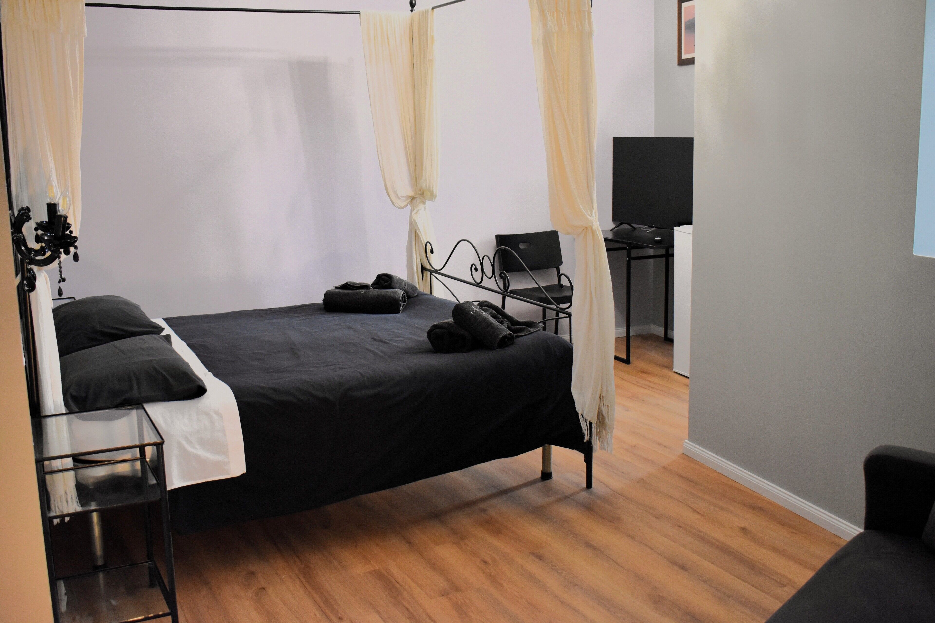 A bedroom with a bed, a bedside table, a chair, and a desk.