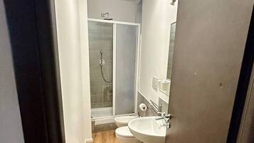 Un couloir étroit mène à une salle de bain équipée d’une douche, de deux lavabos et de toilettes.