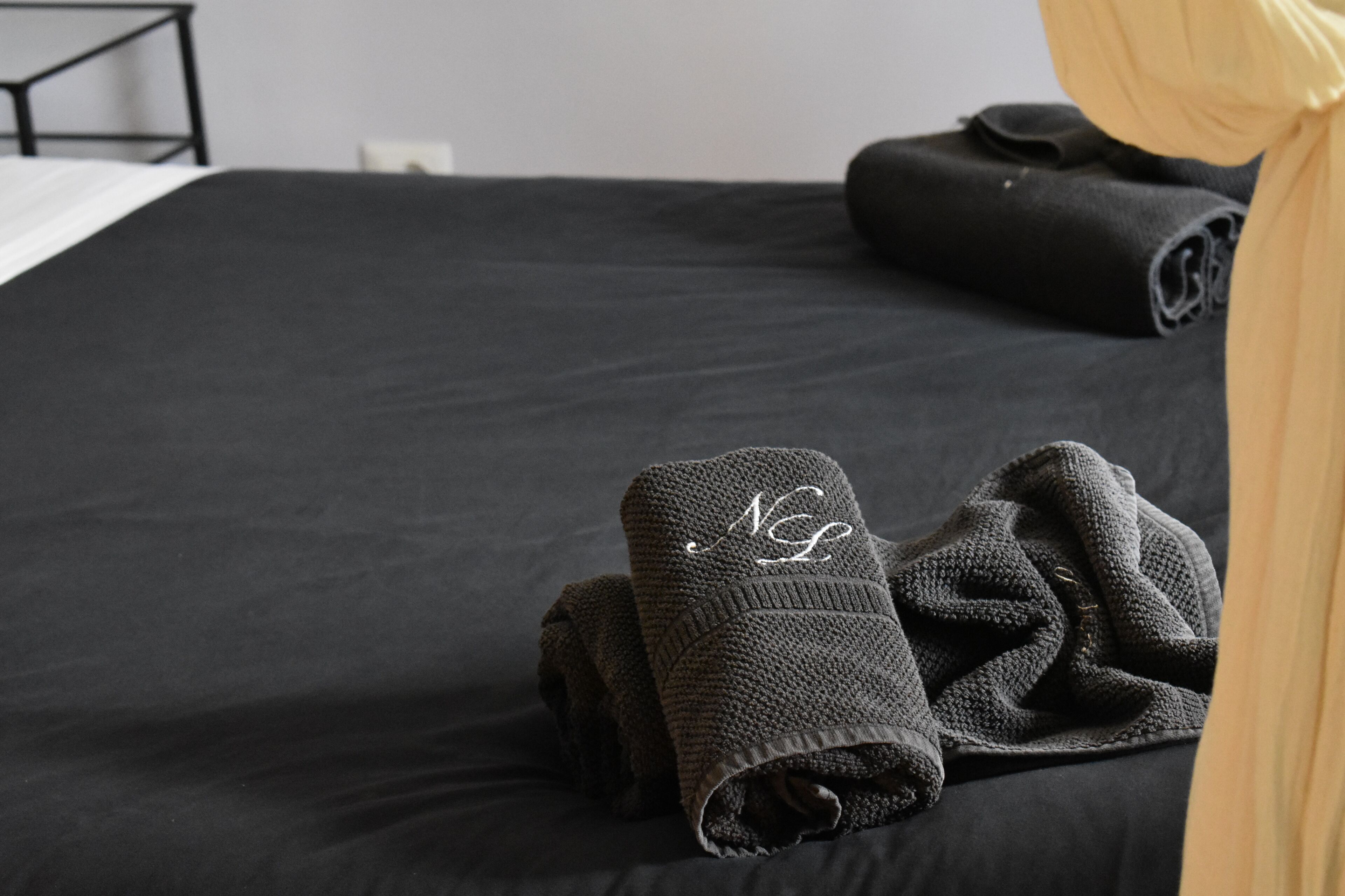 Ein ordentlich bezogenes Bett mit einer schwarzen Tagesdecke und zwei gefalteten Handtüchern mit einem Monogramm.