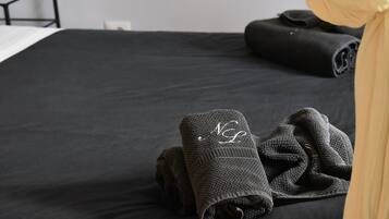 Ein ordentlich bezogenes Bett mit einer schwarzen Tagesdecke und zwei gefalteten Handtüchern mit einem Monogramm.