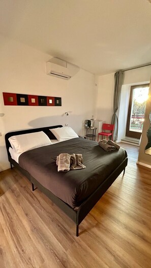 Una cama bien tendida con un cabecero oscuro, una mesita con una silla y una ventana con cortinas.