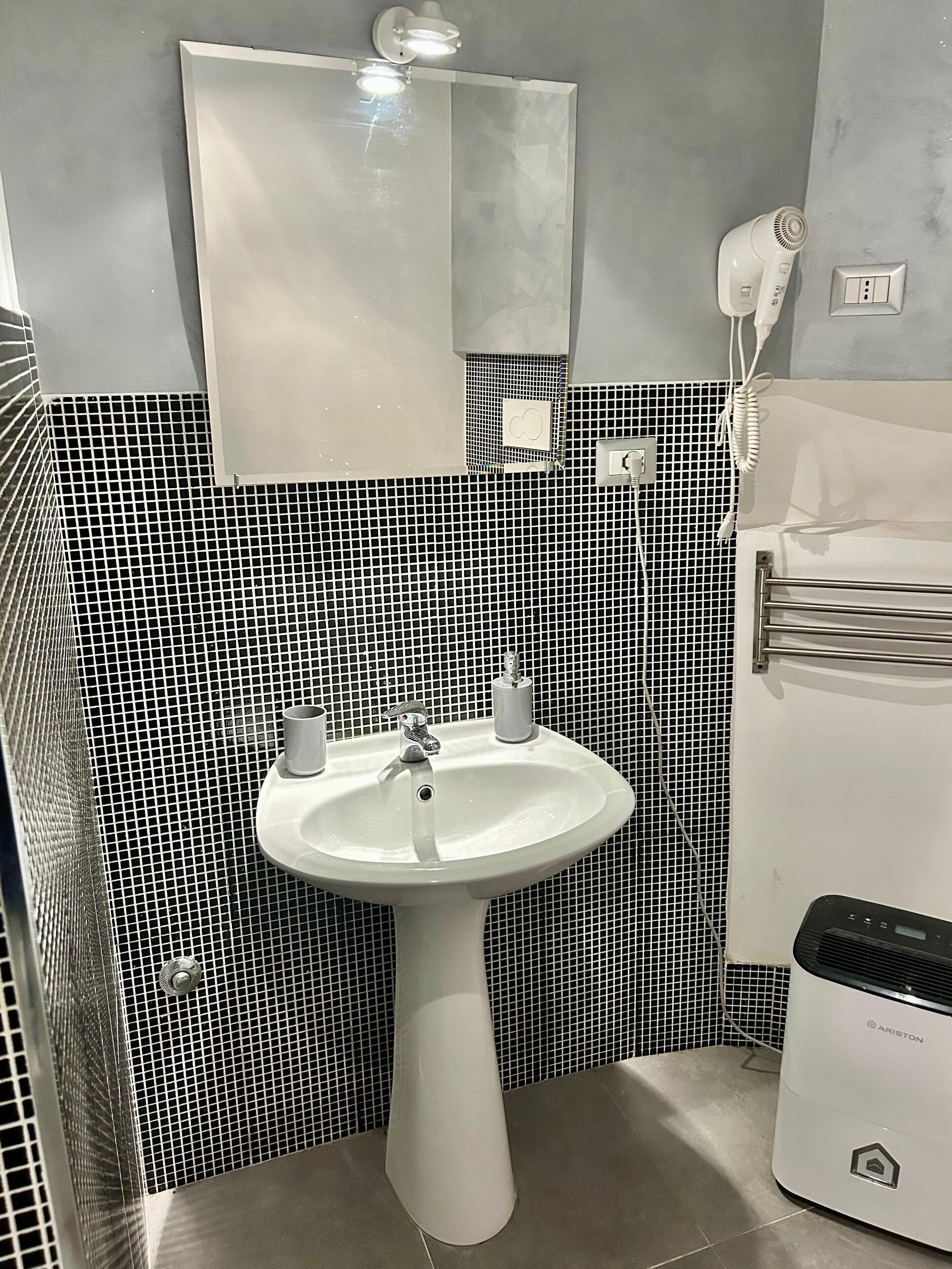 Ein Badezimmer mit Waschbecken, Spiegel, Fön und Heizung.