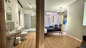 Un baño moderno con lavamanos, inodoro y ducha. La habitación tiene una cama, mesita de noche y televisor.
